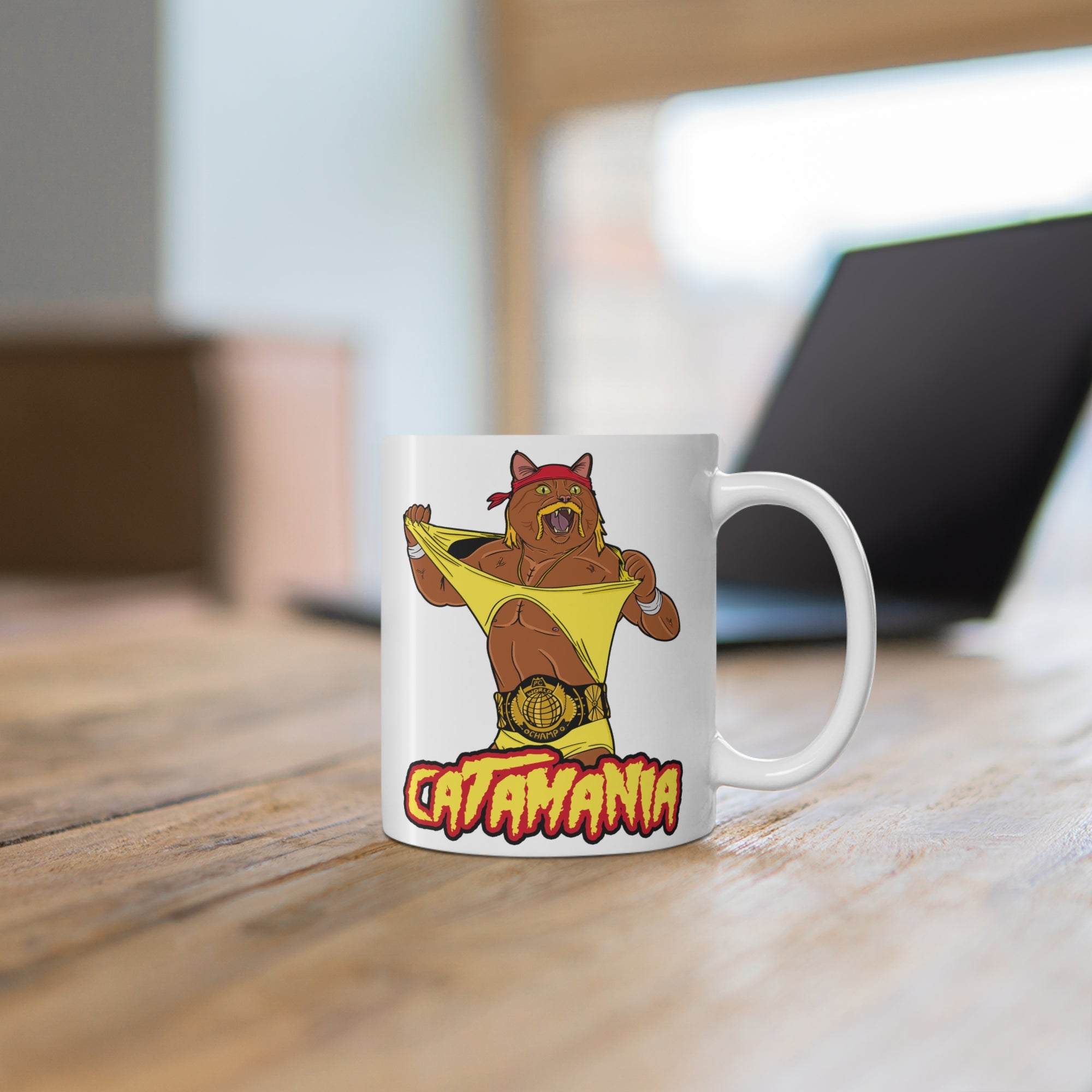Mug with a pro wrestling cat design labeled 'Catamania' on a wooden surface.