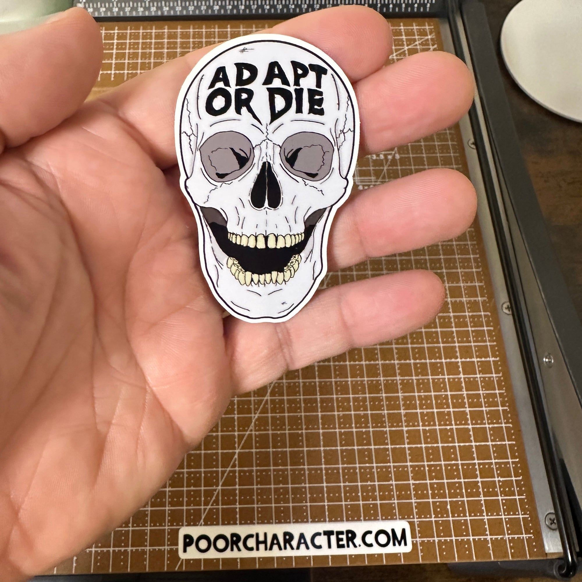 Sticker of A skull with the words 'Adapt or Die' carved into the forehead