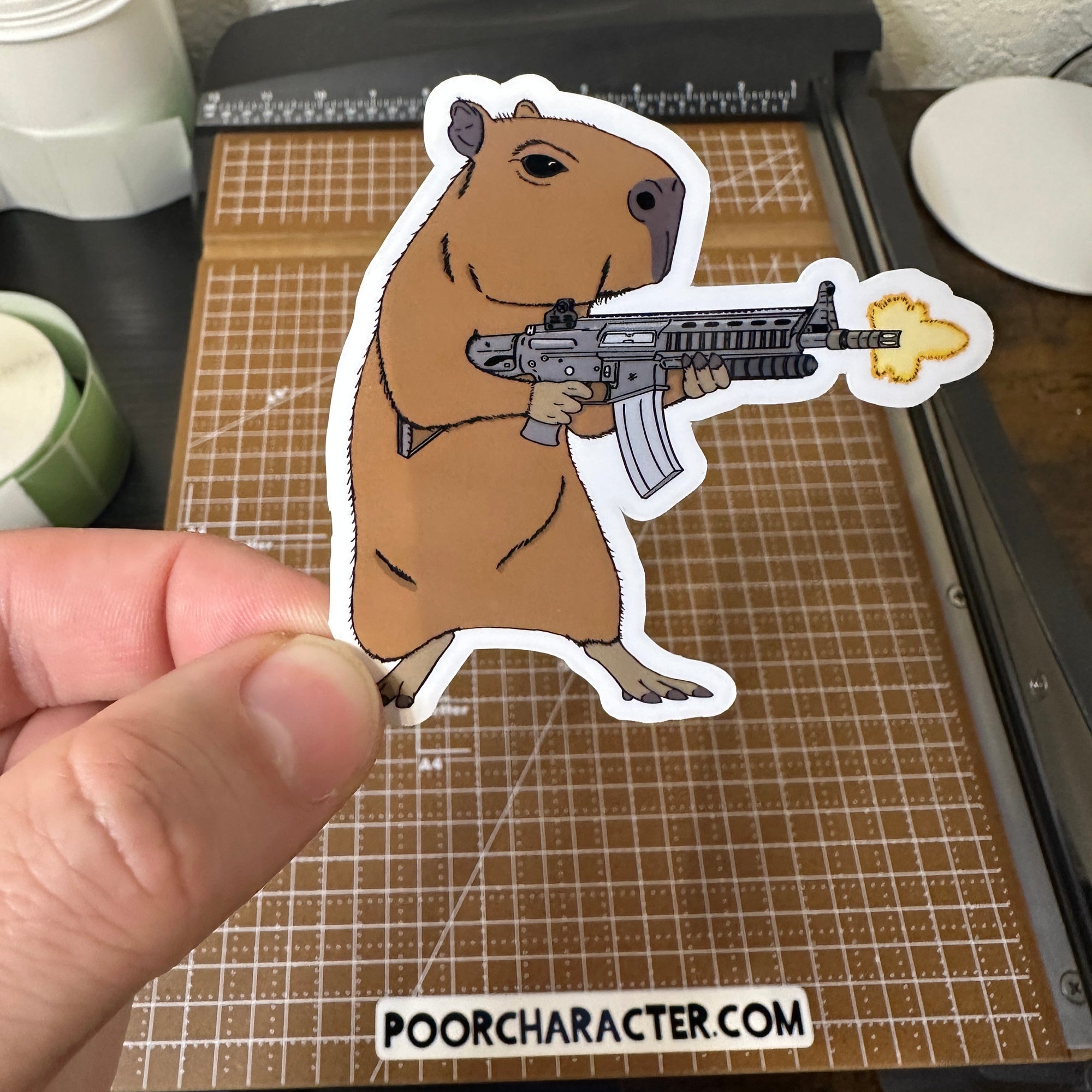 Sticker of a calm capybara firing a large assault rifle, illustrated in a humorous, deadpan combat pose.