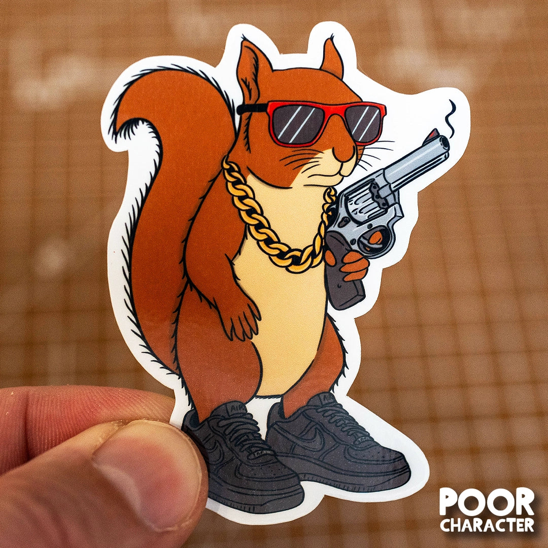 Sticker of a stylized squirrel wearing sunglasses, a chain, and holding a gun, held by a hand on a grid background.
