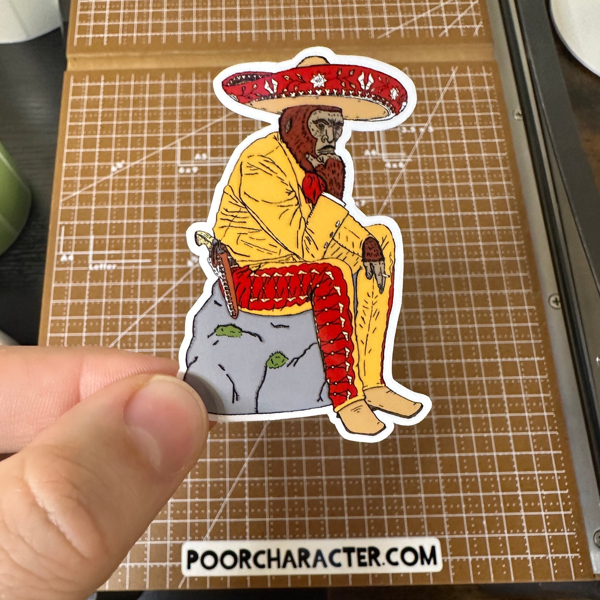 Sticker of A Sasquatch in Mexican Charro gear, sitting on a rock smoking and thinking